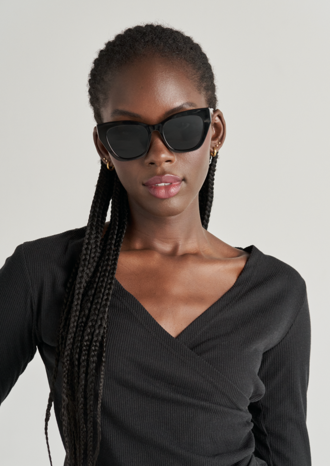 Woman with long braids wears KayTran Eyewear Harper - Polished Black sunglasses and a black V-neck top.