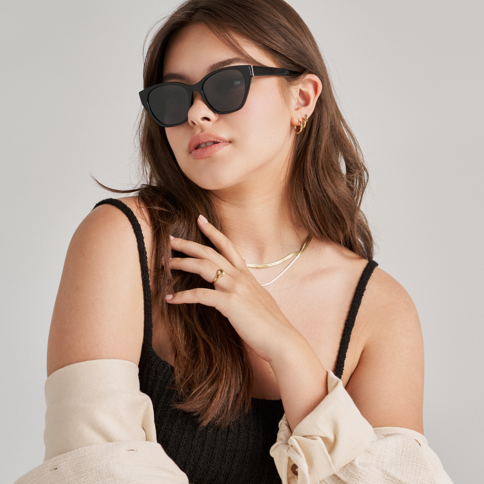 Woman wears KayTran Eyewears Taylor - Polished Black sunglasses, black top, gold jewelry, and beige sweater draped over shoulders.