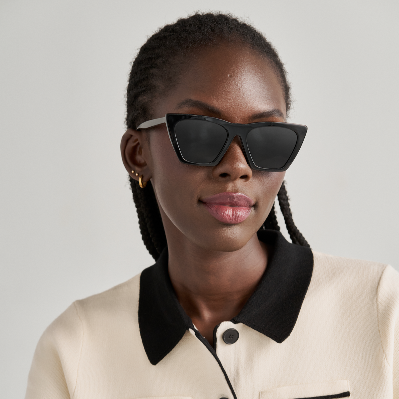 Woman with braided hair wears KayTran Eyewears Frankie - Polished Black cat-eye sunglasses and a cream top.