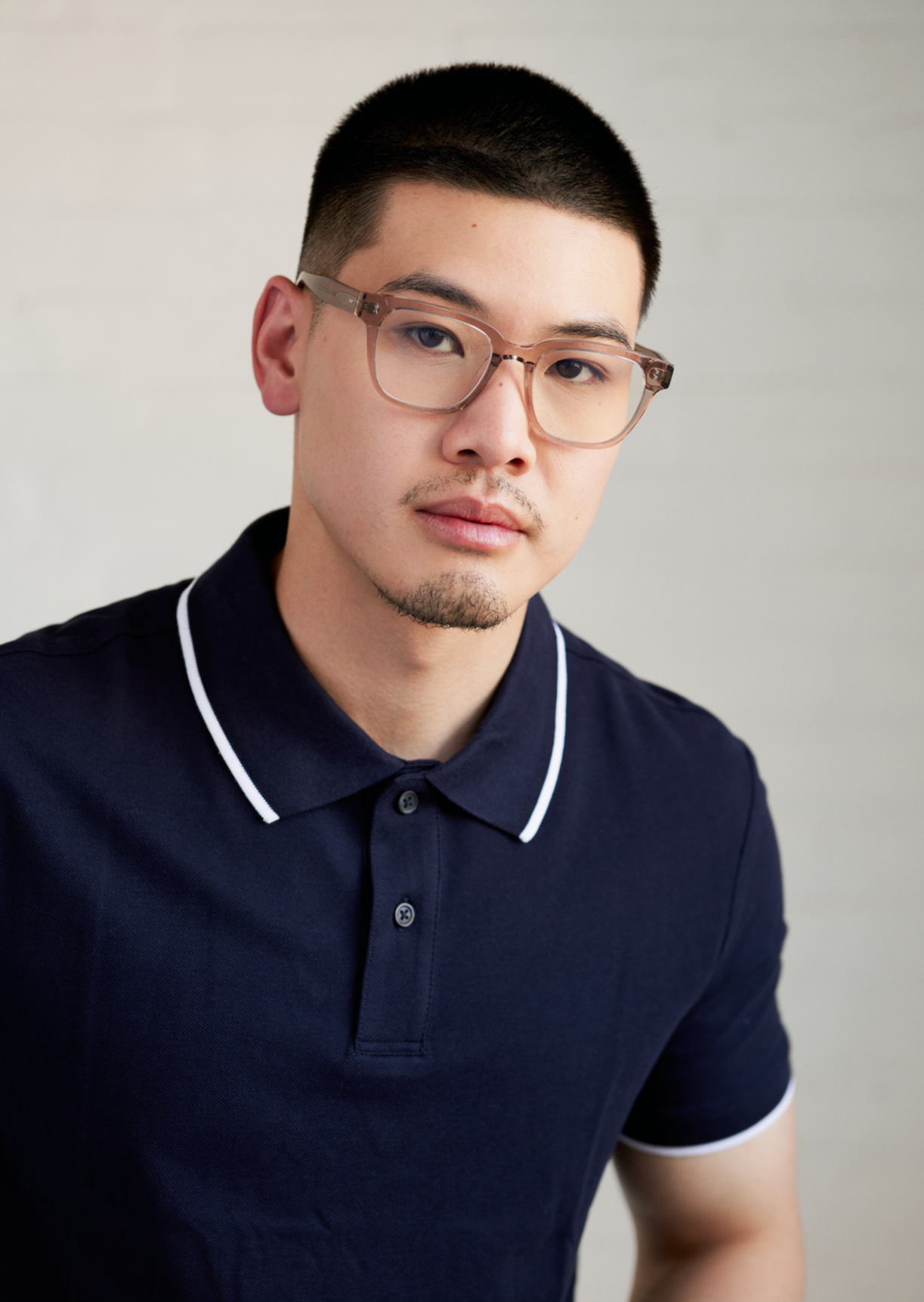A man models KayTran Eyewears Charlie Optical - Stone Taupe glasses, wearing a navy polo against a light background.