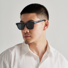 Man with short hair wearing KayTran Eyewears Charlie - Dark Denim sunglasses and a white shirt, looking to the side.