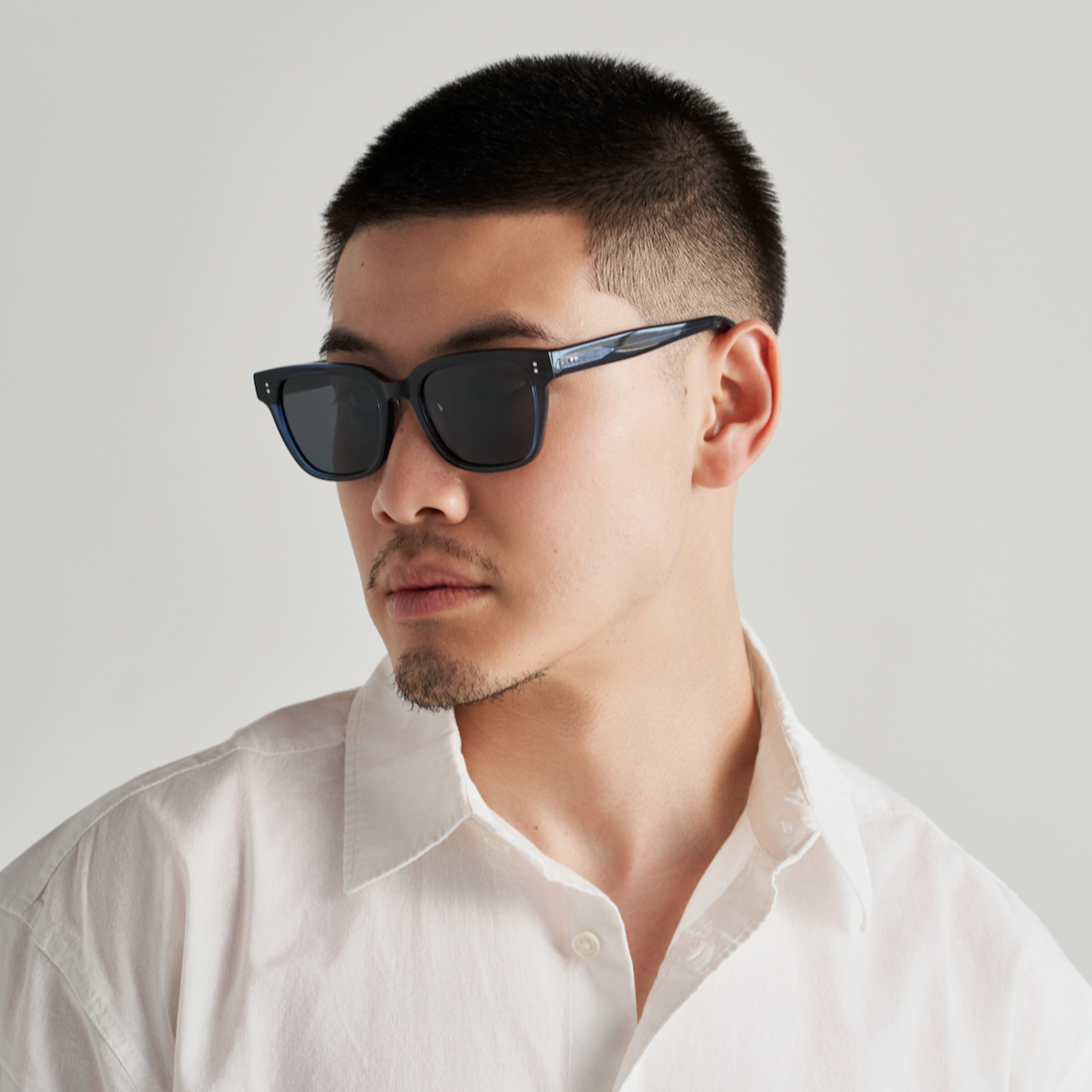 Man with short hair wearing KayTran Eyewears Charlie - Dark Denim sunglasses and a white shirt, looking to the side.