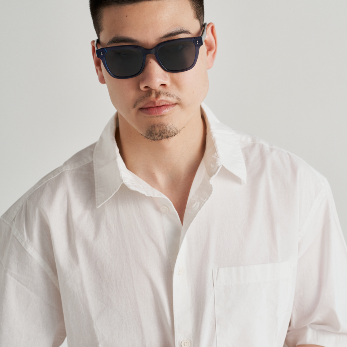 Man wears KayTran Eyewears Charlie - Dark Denim sunglasses and a white short-sleeve shirt, facing the camera.