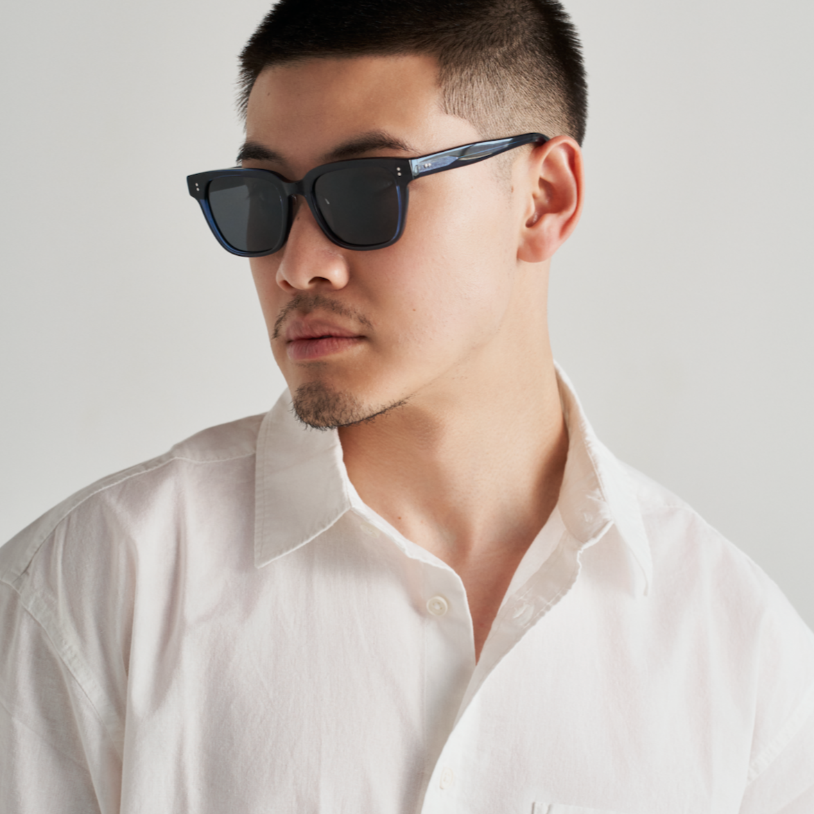 Man wears KayTran Eyewears Charlie - Polished Black sunglasses, looking sideways against a plain light background.