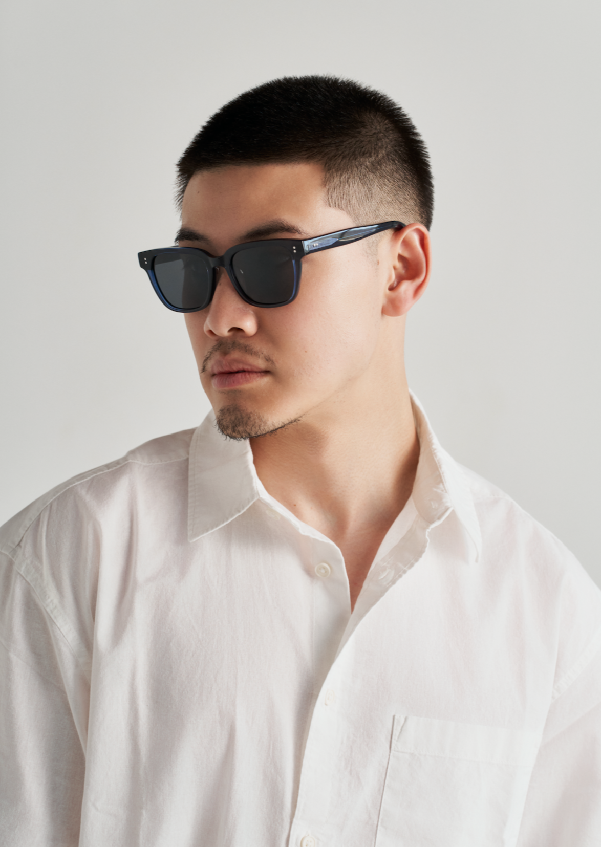 Man wears KayTran Eyewears Charlie - Polished Black sunglasses, looking sideways against a plain light background.