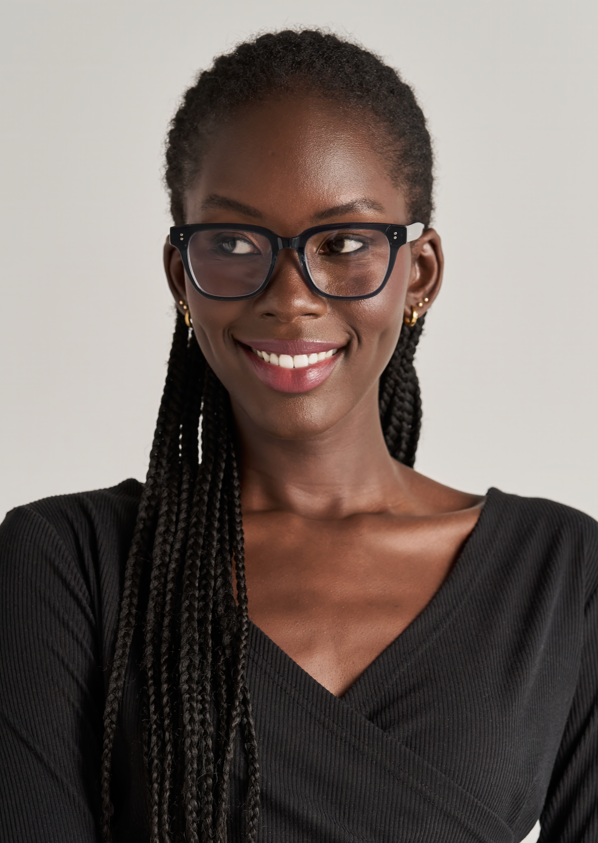 Woman with long braids in KayTran Eyewear’s Charlie Optical - Polished Black, smiling and looking to the side.