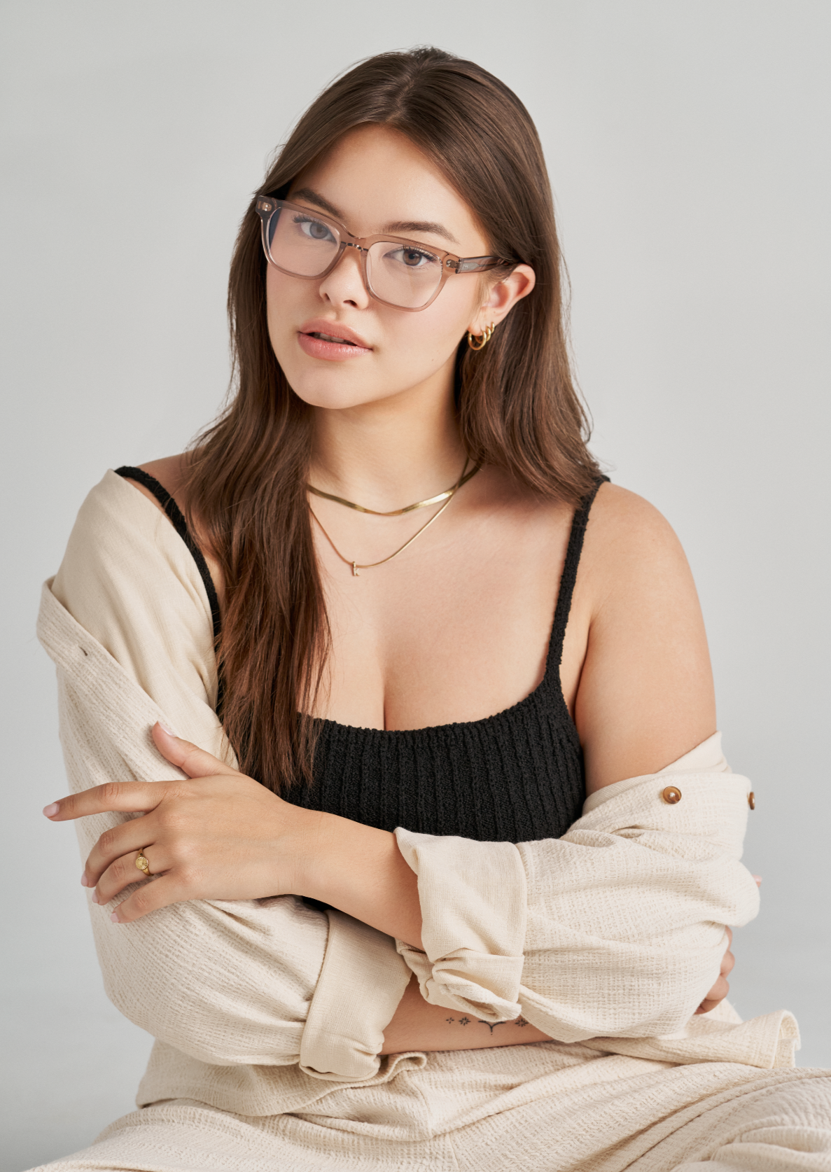 Woman with long brown hair wears KayTran Eyewears Charlie Optical - Stone Taupe glasses, black top, and cream jacket.