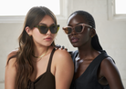 Two women in sleeveless tops wear KayTran Eyewears Harper - Olive sunglasses, posing indoors against a light background.
