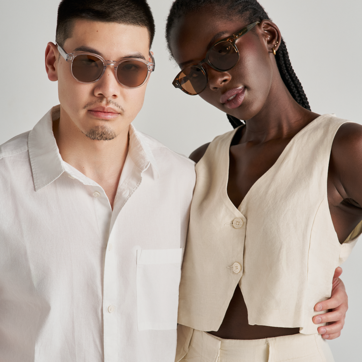 Two people wear KayTran Eyewears Reese - Amber Honey sunglasses, posing together in light, neutral outfits.