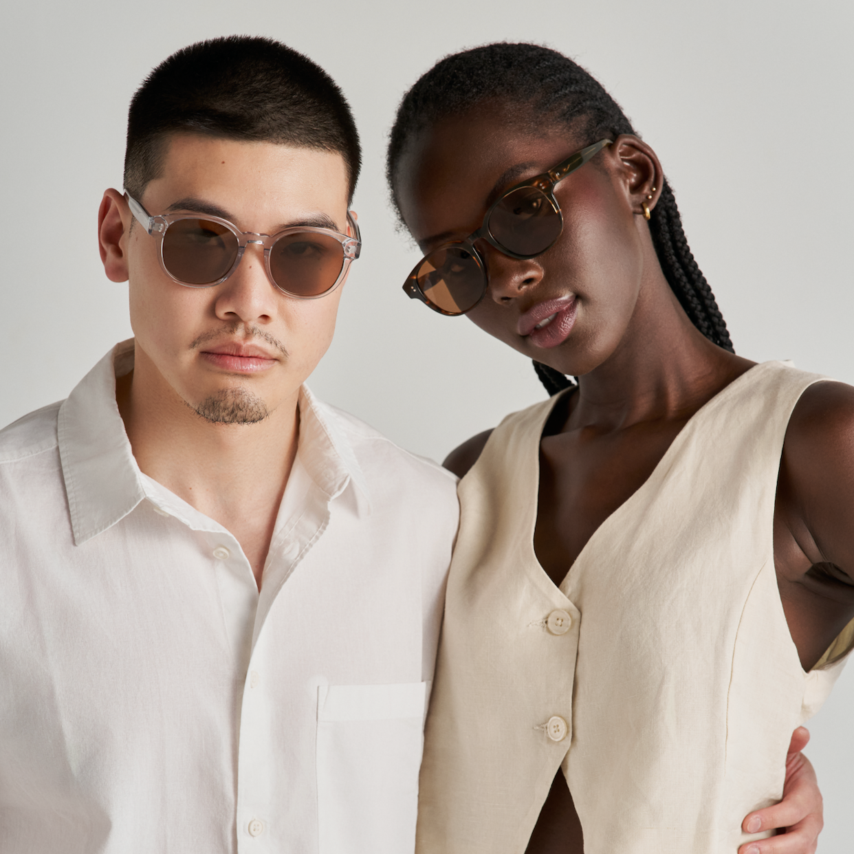 Two people wear KayTran Eyewears Reese - Fog sunglasses, dressed in light clothing against a plain background.