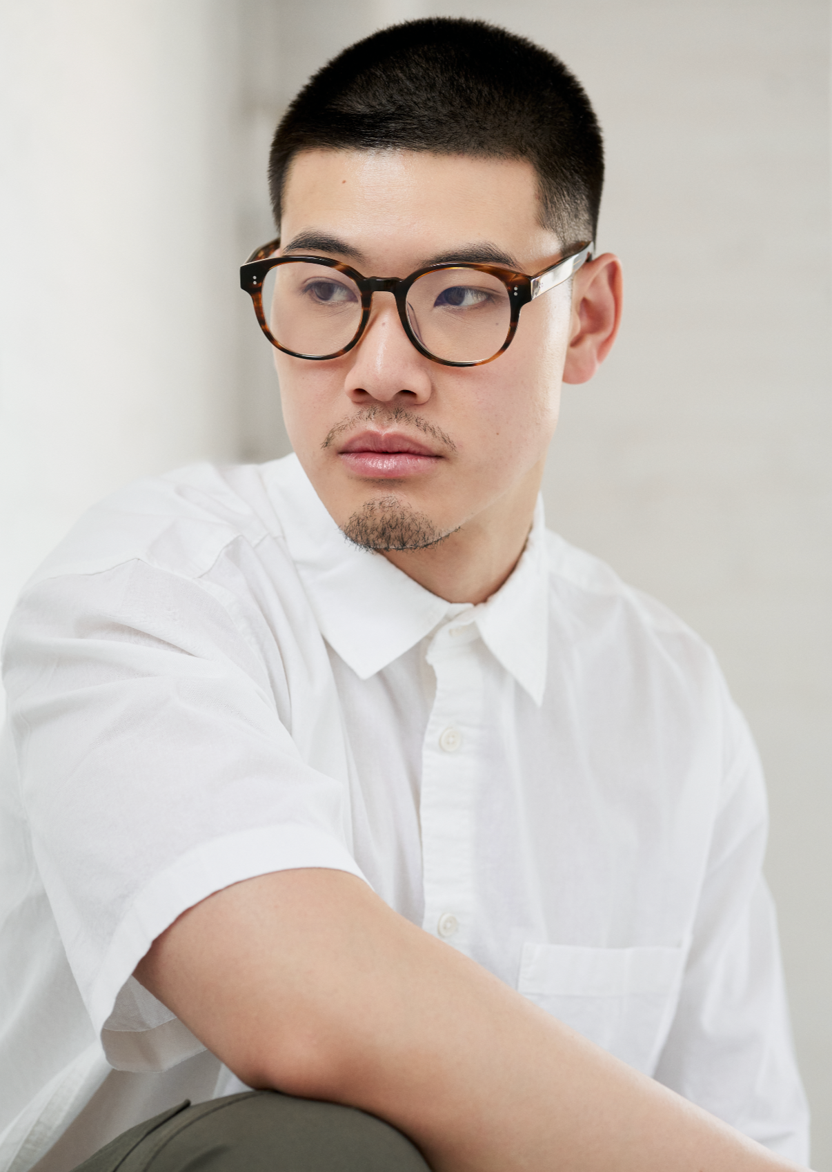 Man wears KayTran Eyewear Reese Optical - Polished Black glasses, looking to the side against a light background.