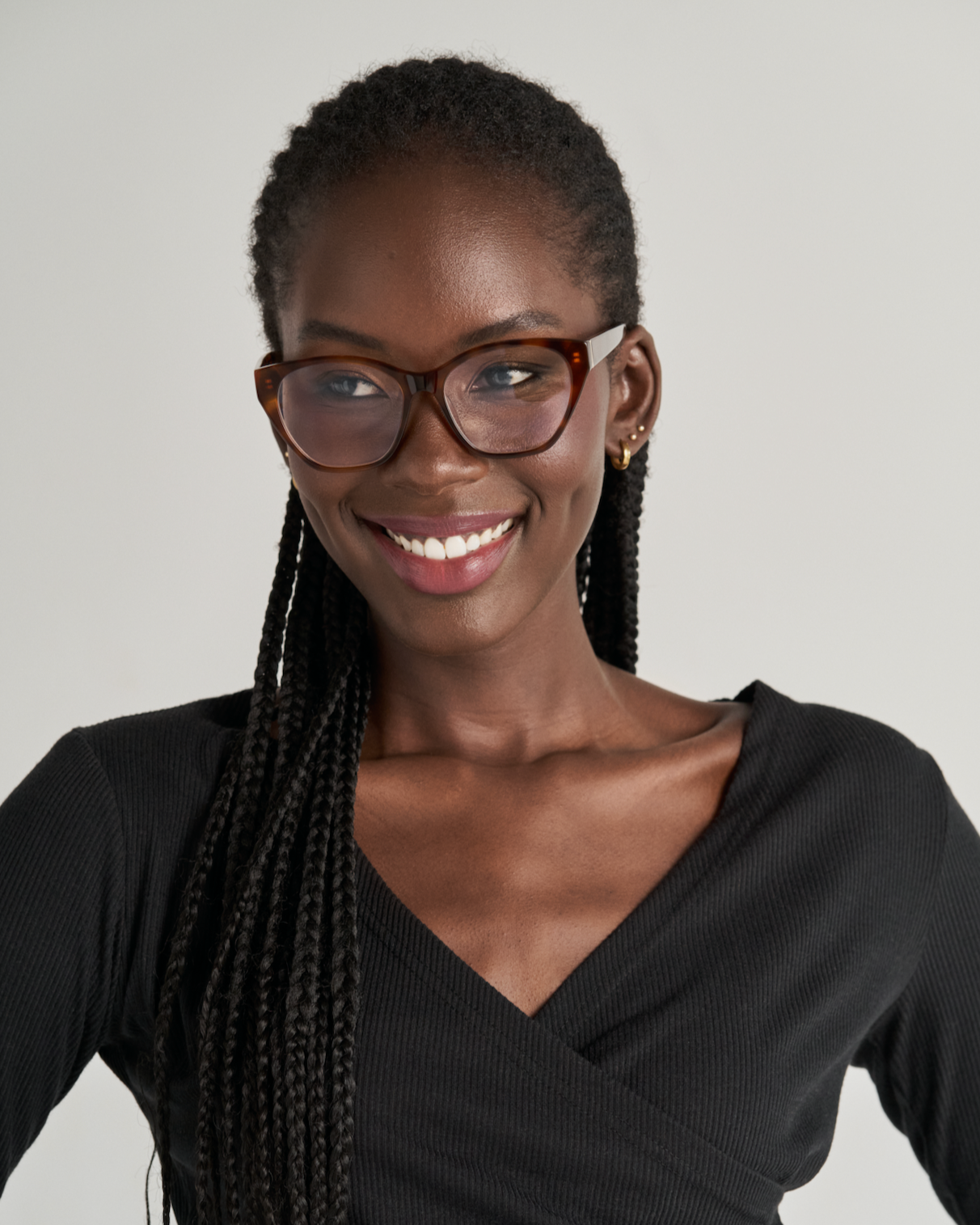Smiling woman with braided hair wears KayTran Eyewears Taylor Optical - Honey Tort and a black long-sleeve top.