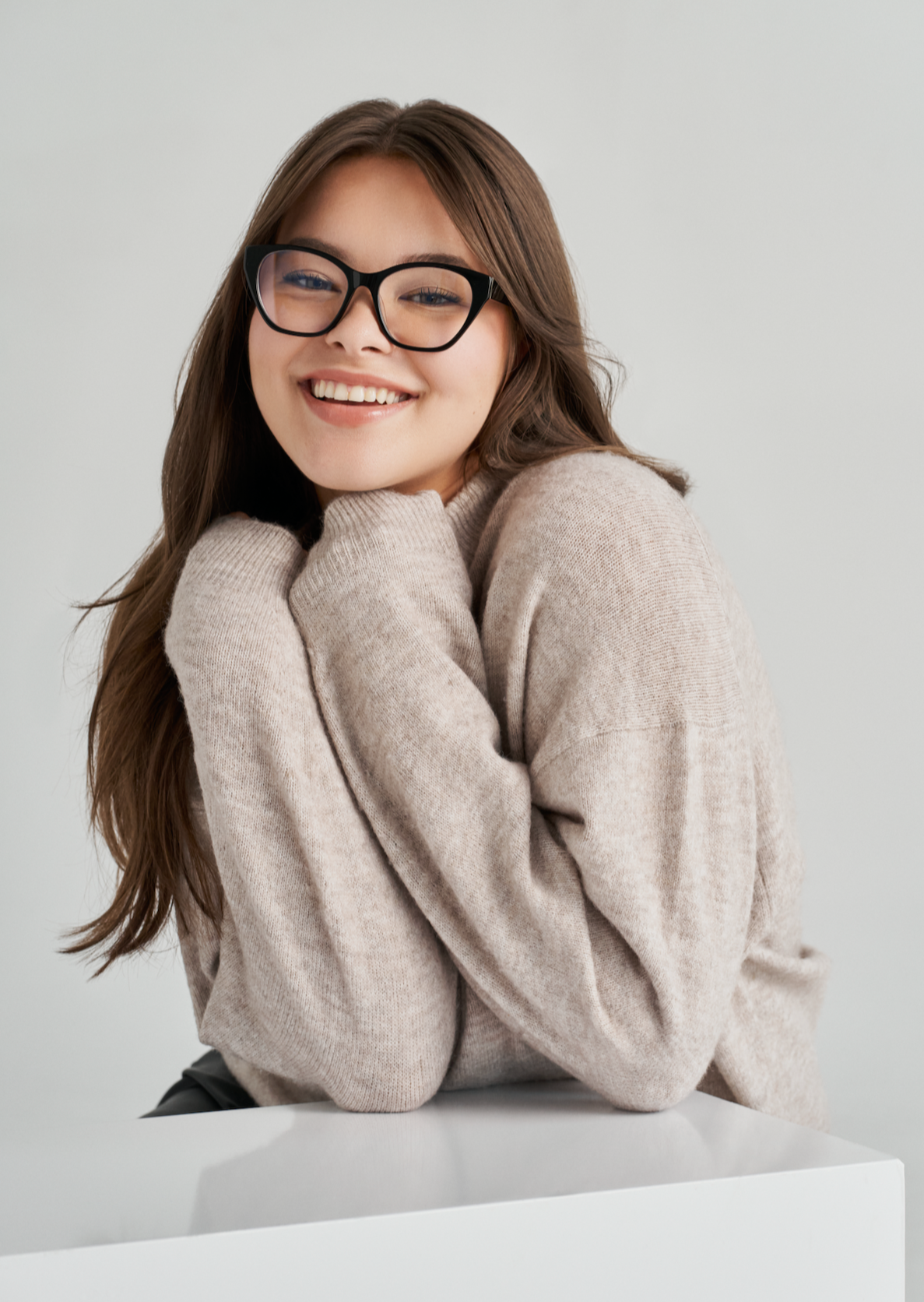 Woman with long brown hair smiles in KayTran Eyewears Taylor Optical - Polished Black glasses and a beige sweater.