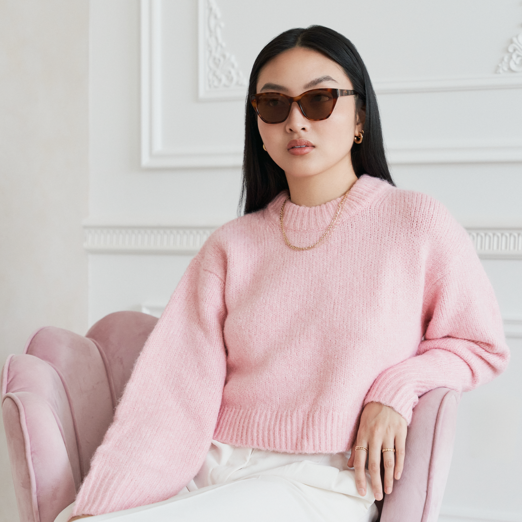 Woman wearing KayTran Eyewears Taylor - Honey Tort sunglasses sits on a pink chair in an elegant white room.