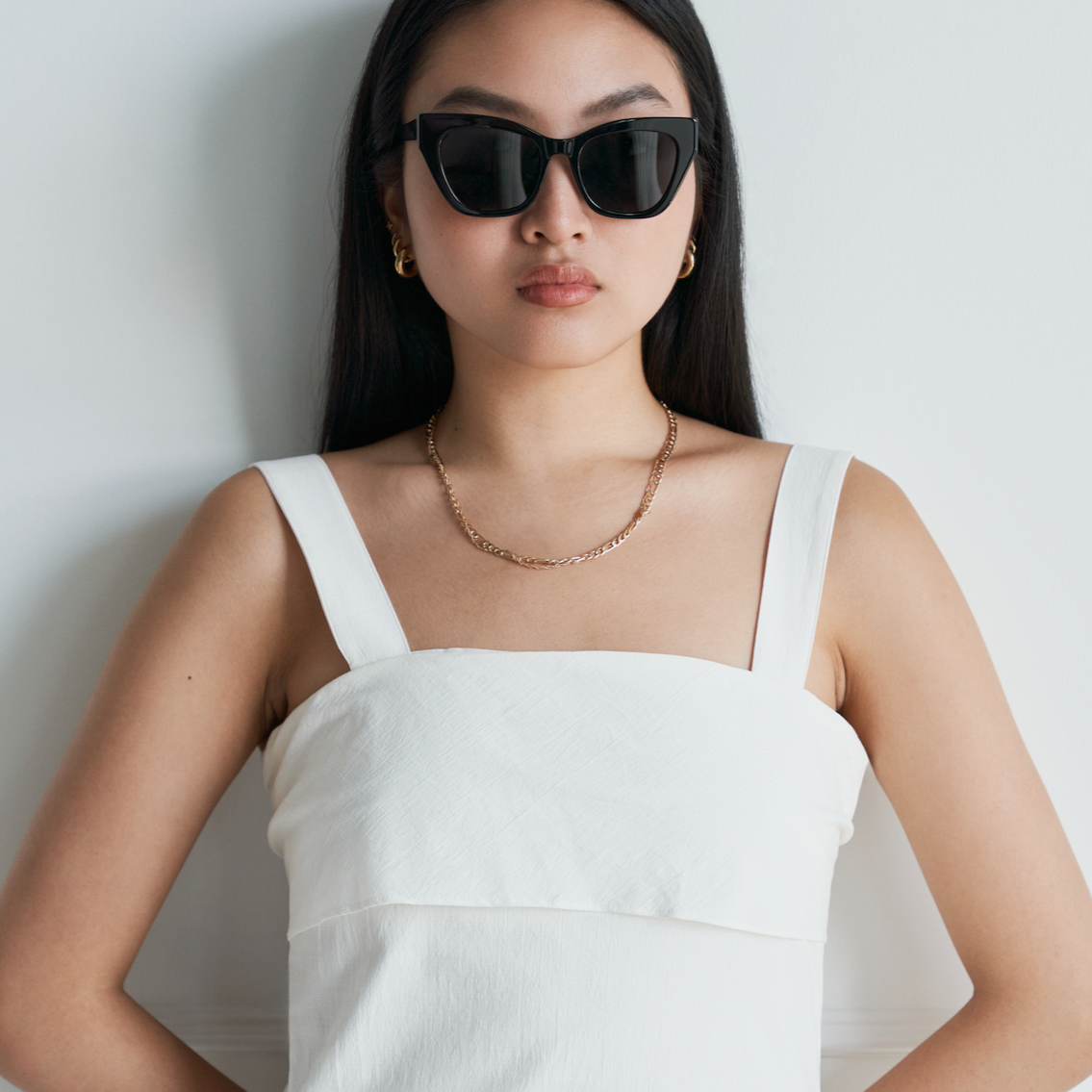 Woman with long dark hair wears KayTran Eyewears Harper - Polished Black sunglasses, a white dress, and gold necklace.