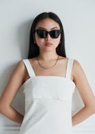 Woman with long dark hair wears KayTran Eyewears Harper - Polished Black sunglasses, a white dress, and gold necklace.