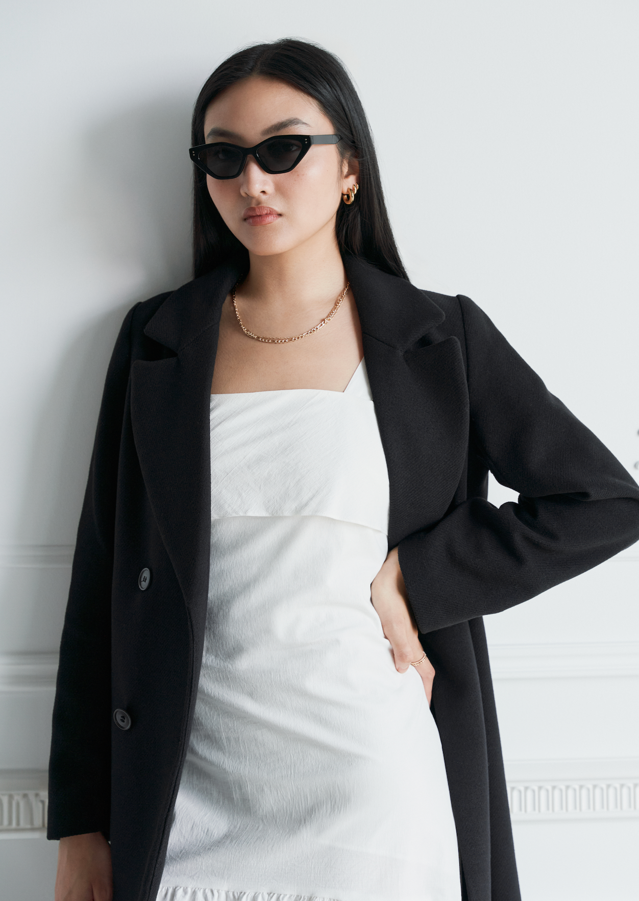 Woman in a black coat and white dress wears KayTran Eyewear Naomi - Polished Black sunglasses and gold jewelry.