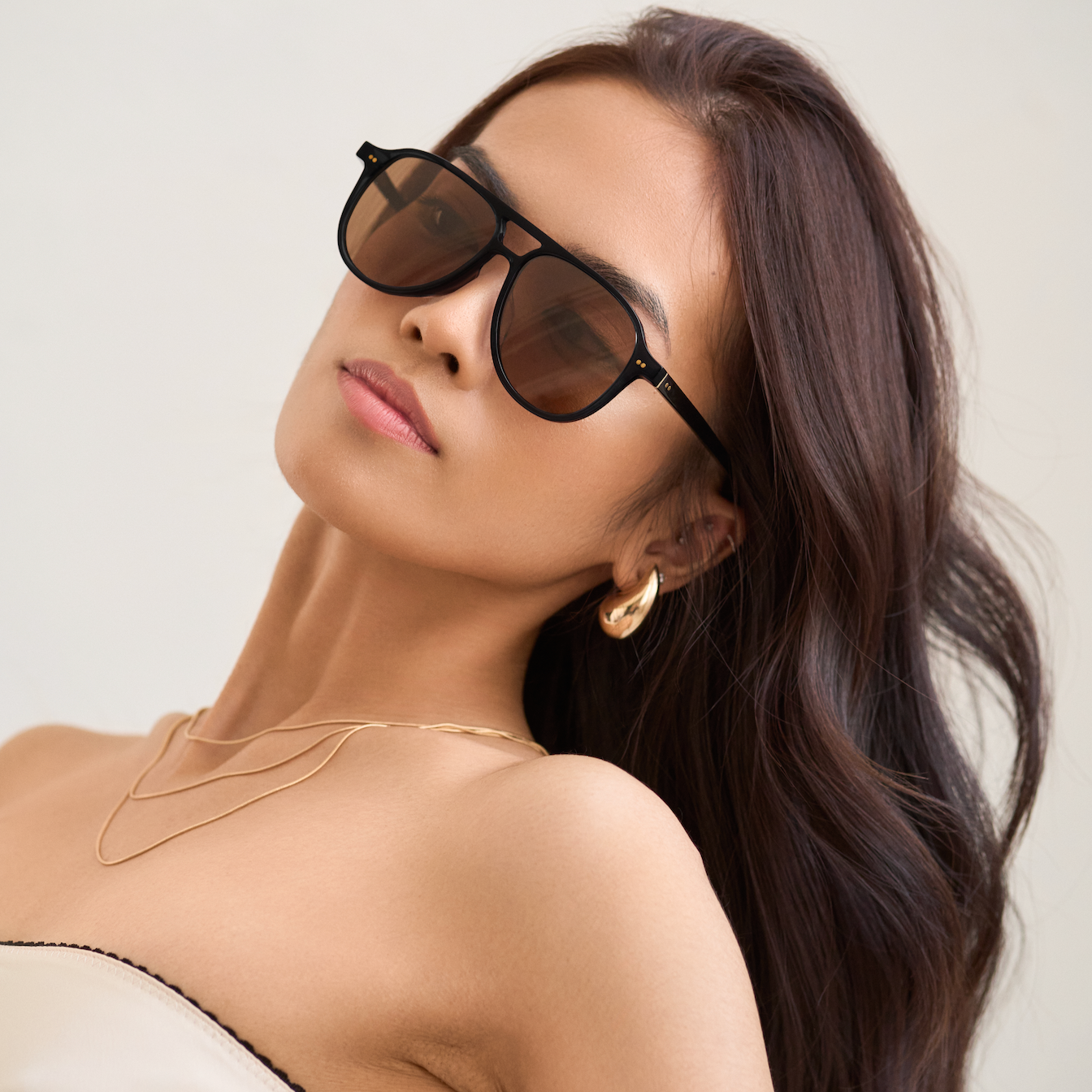Woman with long brown hair wears KayTran Eyewears Knox - Black & Brown Lens sunglasses against a light background.