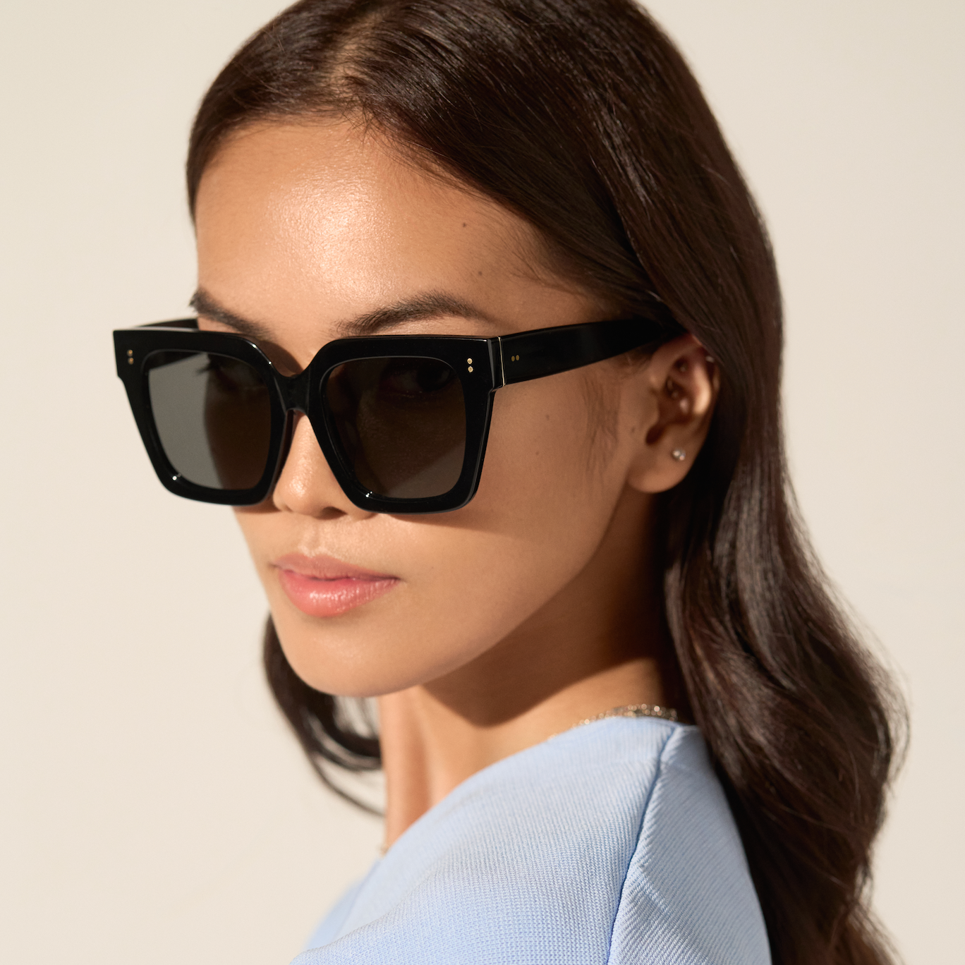 Woman with long brown hair wears KayTran Eyewear Logan - Polished Black sunglasses and a light blue top.