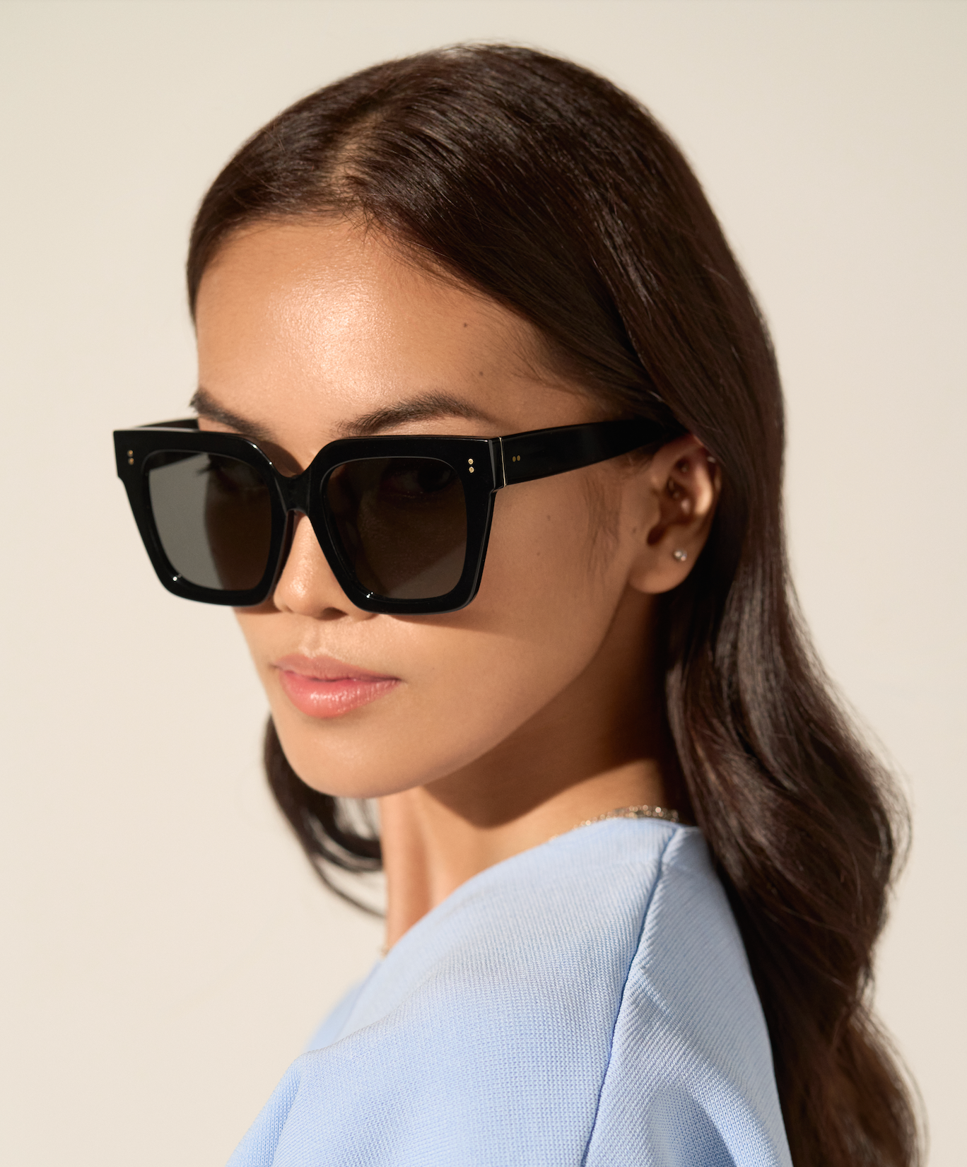 Woman with long brown hair wears KayTran Eyewear Logan - Polished Black sunglasses and a light blue top.