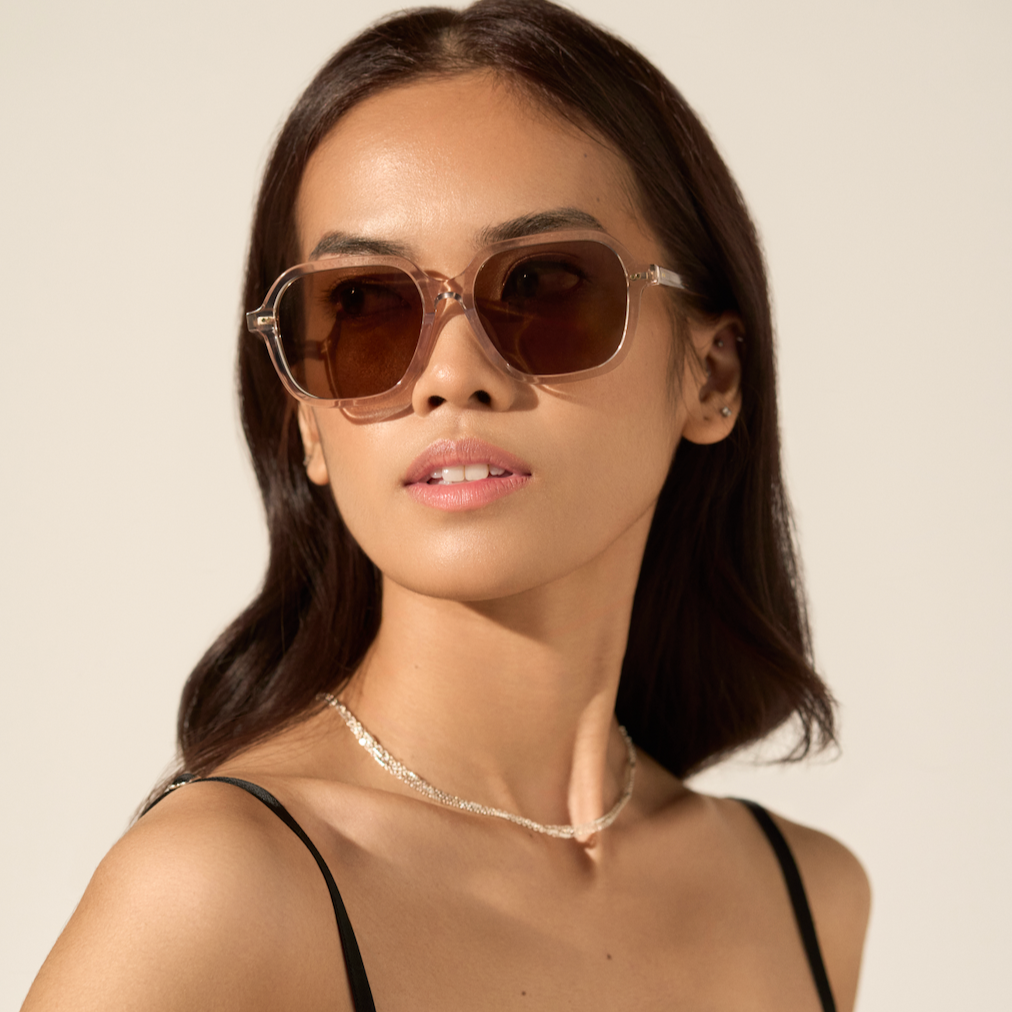 Woman wearing KayTran Eyewear River - Sand sunglasses, silver necklace, and black strap top against a neutral background.
