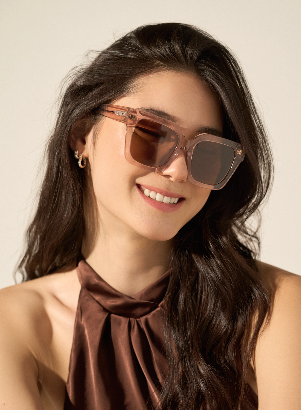 Woman with long dark hair wears KayTran Eyewears Logan - Bloom sunglasses and a brown halter top, smiling.