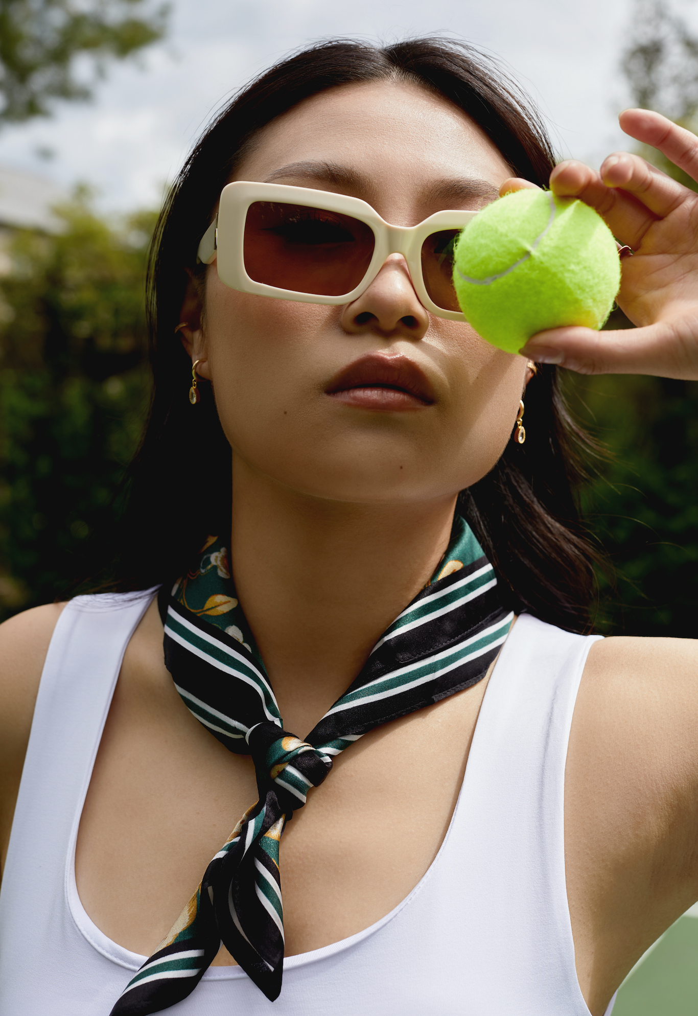 Woman outdoors holds a tennis ball to her eye, wearing KayTran Eyewear Brooks - Ecru sunglasses and a scarf.