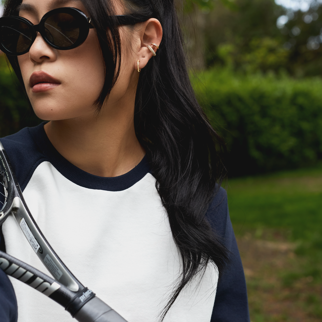 Woman in Mara - Polished Black by KayTran Eyewear, holding a tennis racket and wearing a MANHATTAN, NEW YORK sweatshirt.