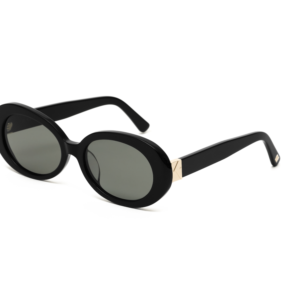 Mara - Polished Black sunglasses by KayTran Eyewear, oval with dark lenses and gold arms, on a white background.