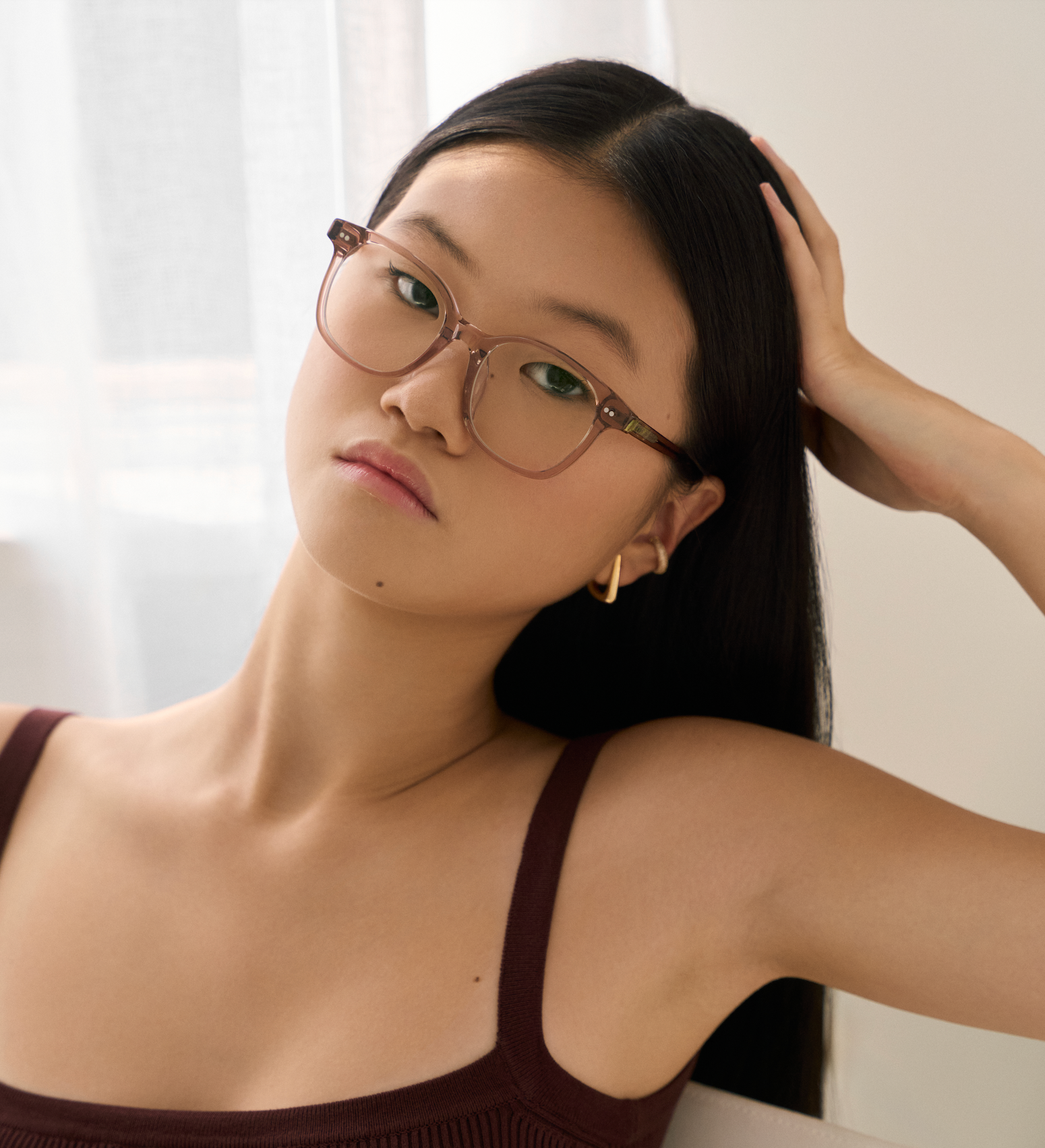 A woman with long dark hair wears KayTran Eyewears Easton - Stone Taupe glasses and a maroon top, looking at the camera.