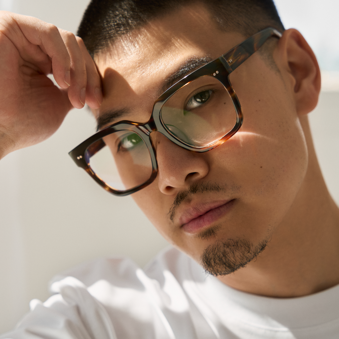 Man with short hair wearing KayTran Eyewear Andy - Amber Honey glasses, hand on forehead, facing camera.