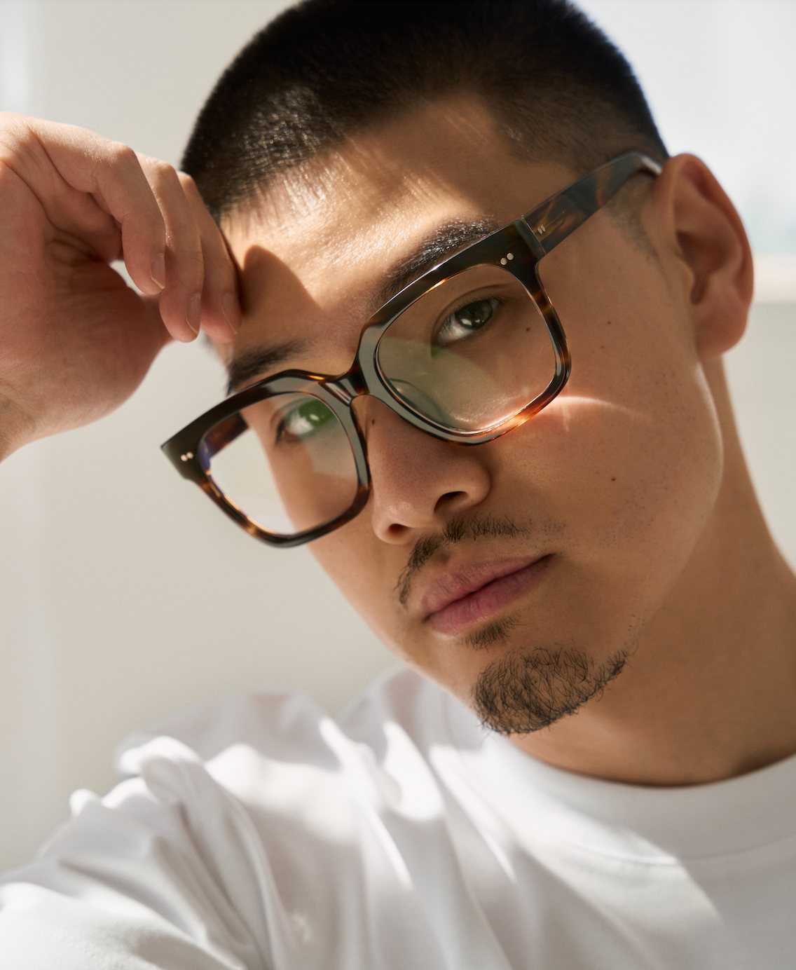 Man with short hair wearing KayTran Eyewear Andy - Amber Honey glasses, hand on forehead, facing camera.