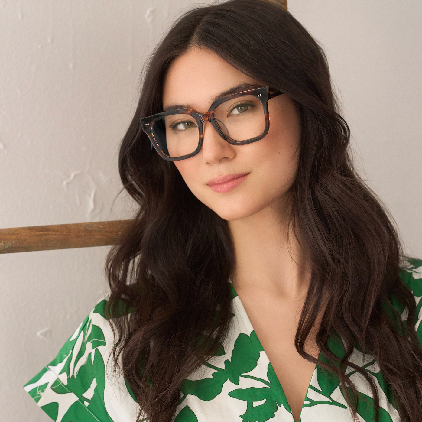 Woman with long dark hair wears KayTran Eyewears Andy - Amber Honey glasses, posed by a neutral wall.