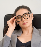 A woman wears KayTran Eyewears Andy - Graphite glasses and a gray blazer, seated with a neutral expression.