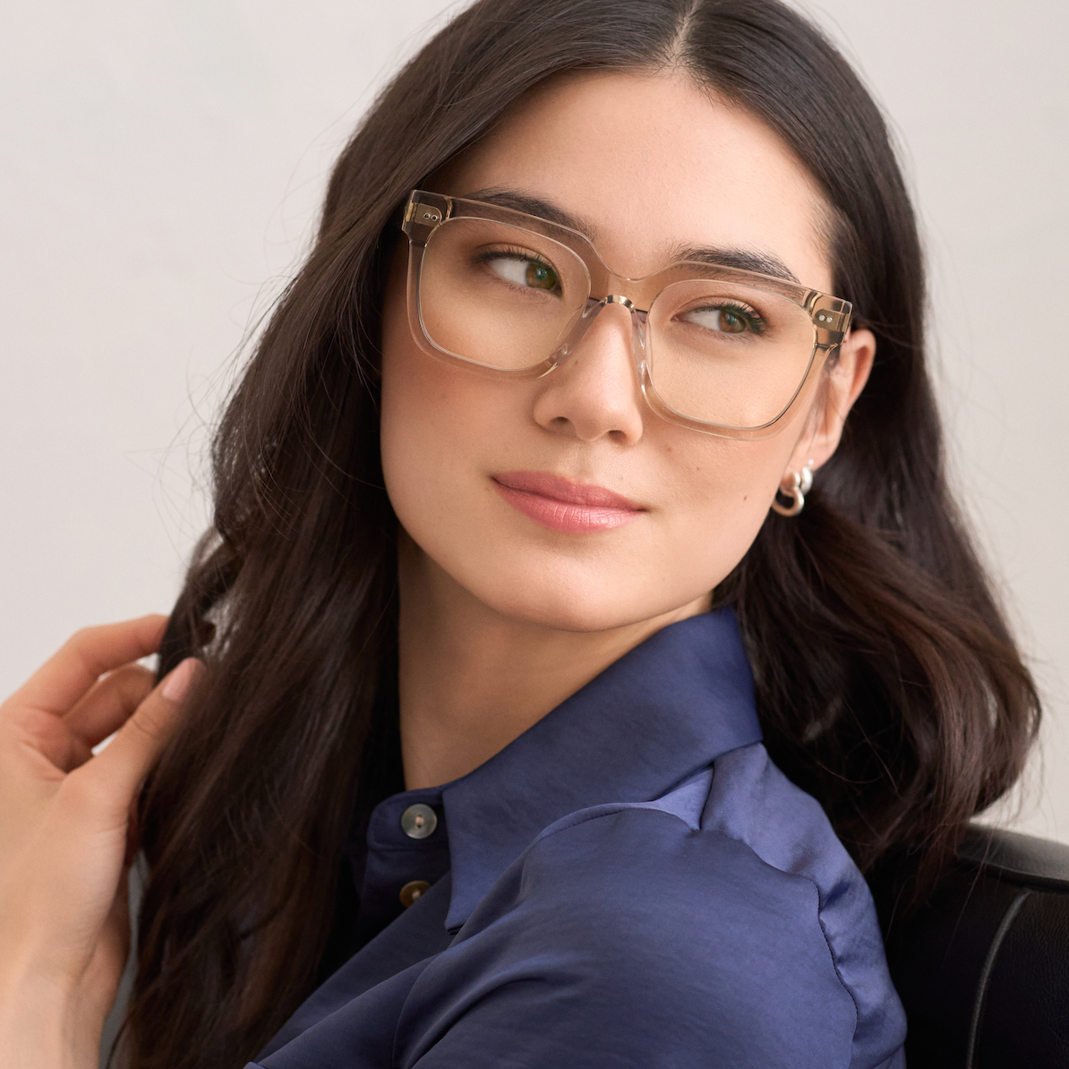 Woman with long dark hair wears KayTran Eyewears Andy - Sand glasses, seated and looking to the side.
