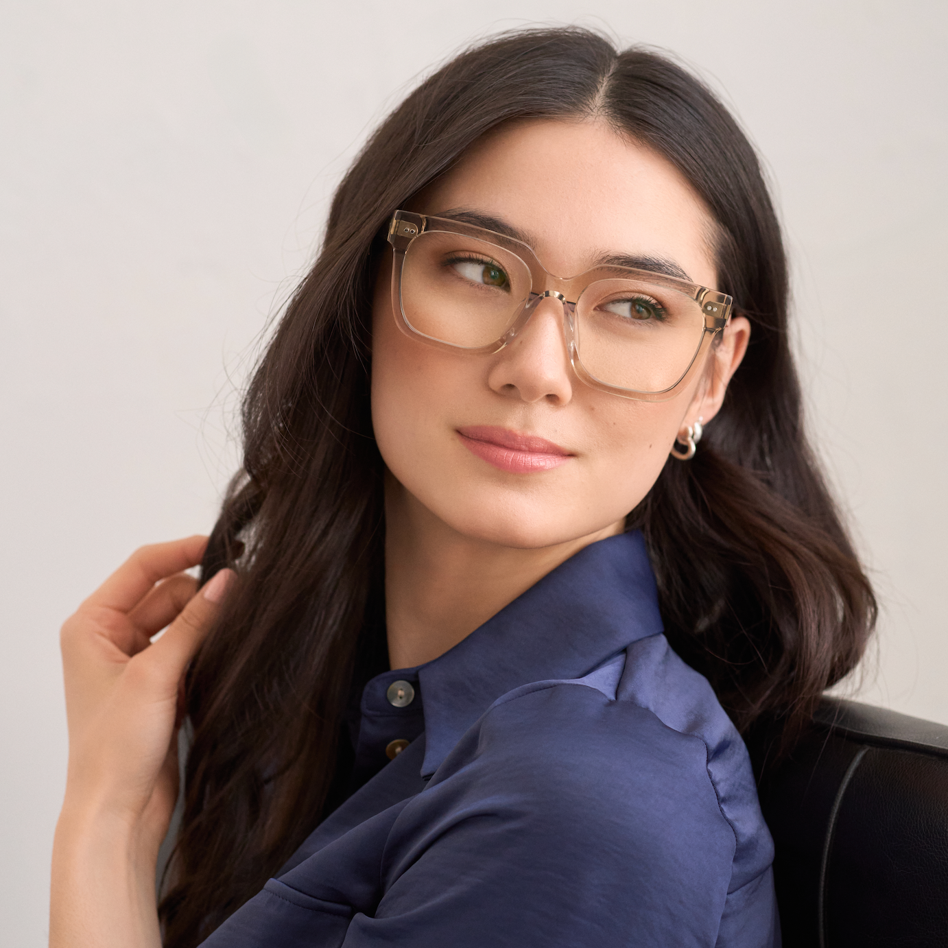 Woman with long dark hair wears KayTran Eyewears Andy - Sand glasses, seated and looking to the side.