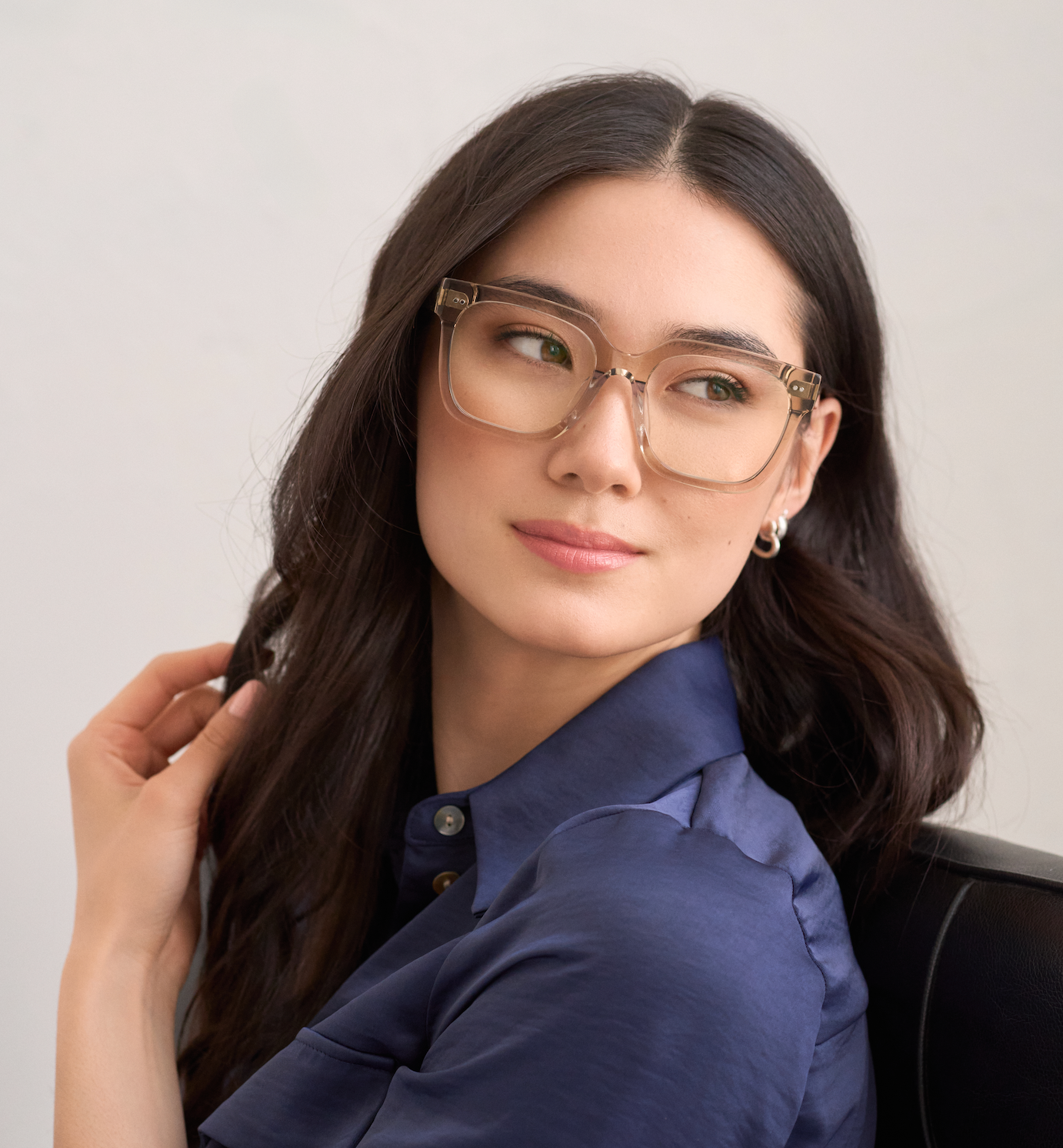 Woman with long dark hair wears KayTran Eyewears Andy - Sand glasses, seated and looking to the side.