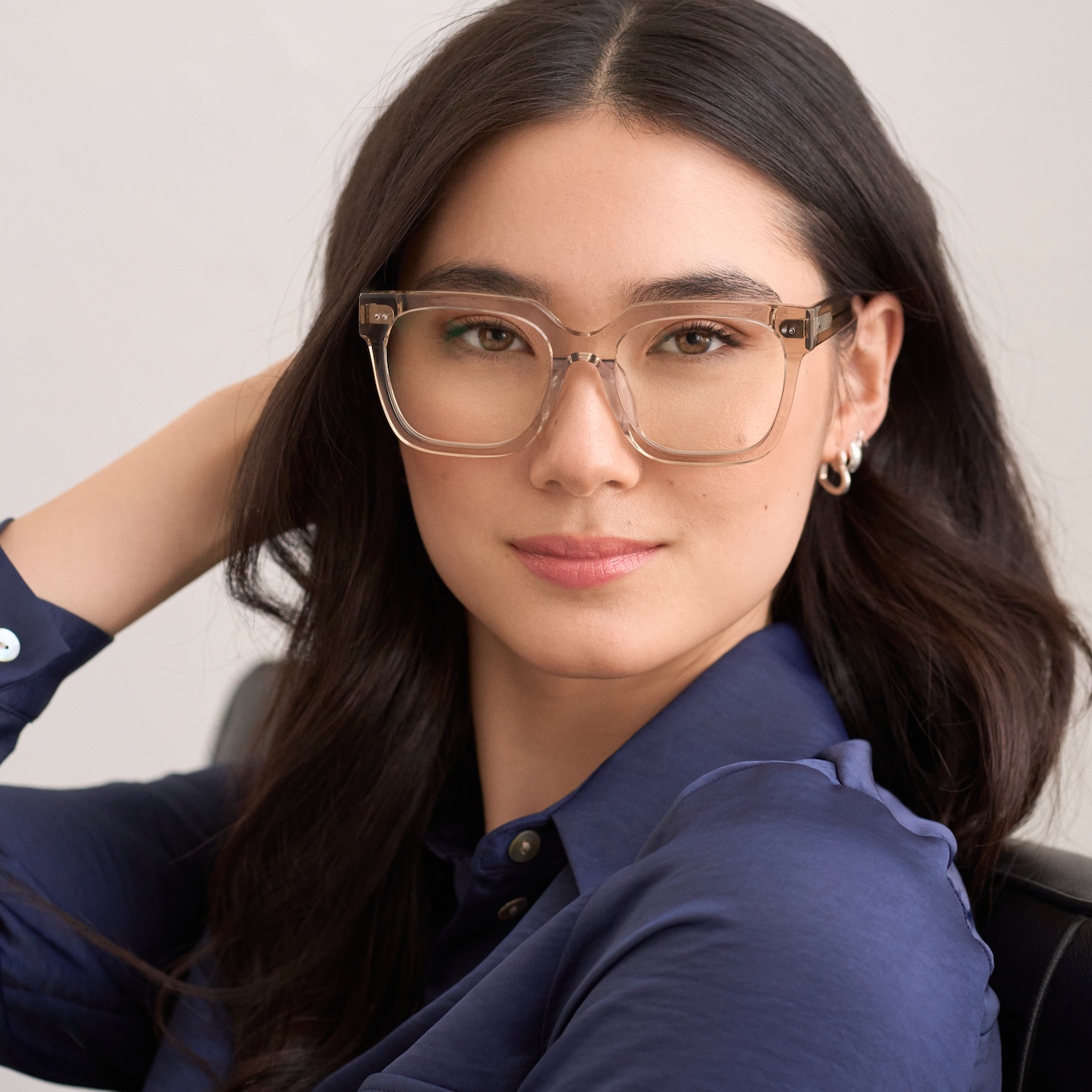 Woman with long dark hair wears KayTran Eyewears Andy - Sand glasses and a navy shirt, looking at the camera.