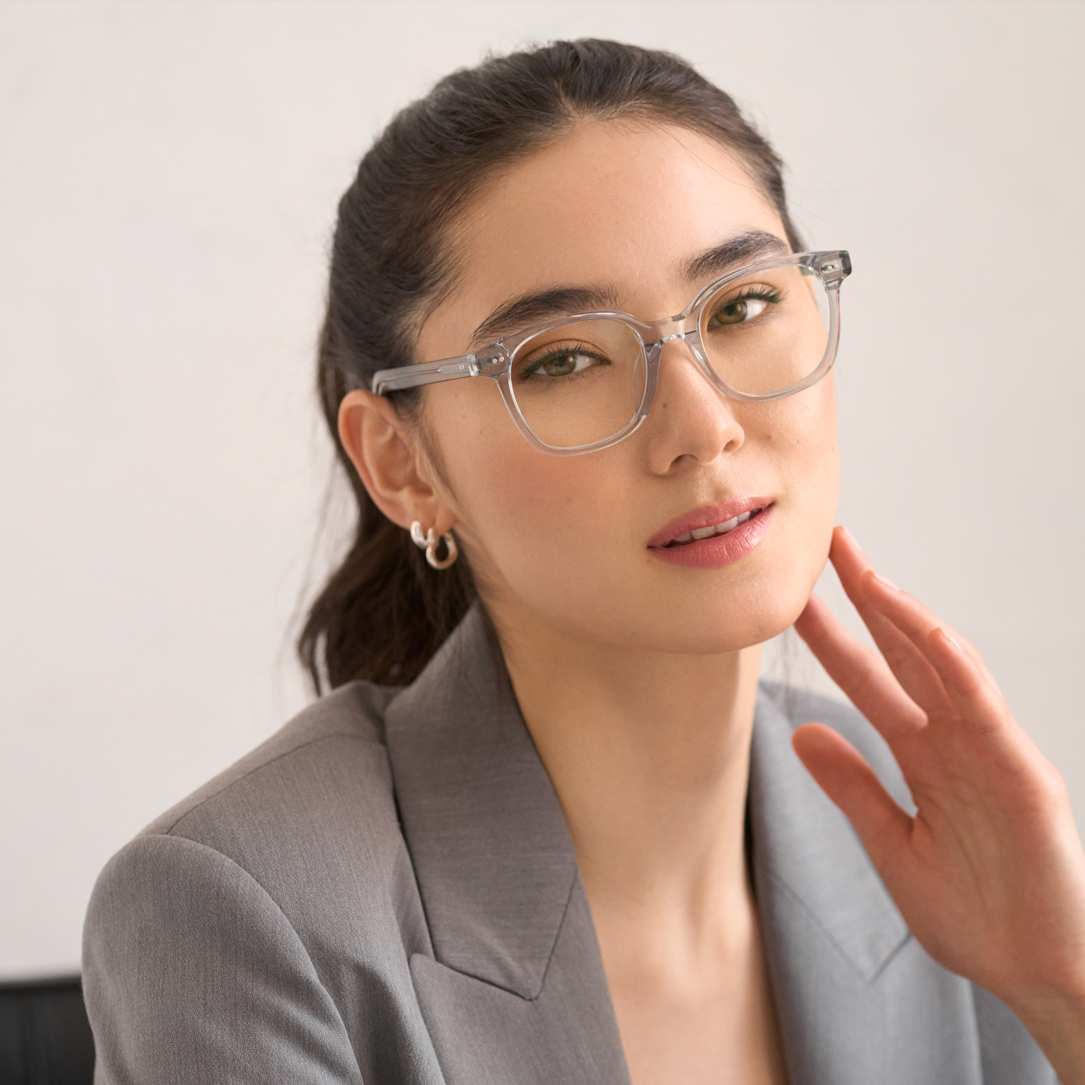Woman with long dark hair in ponytail wears KayTran Eyewear Easton - Cloud clear glasses and a gray blazer.