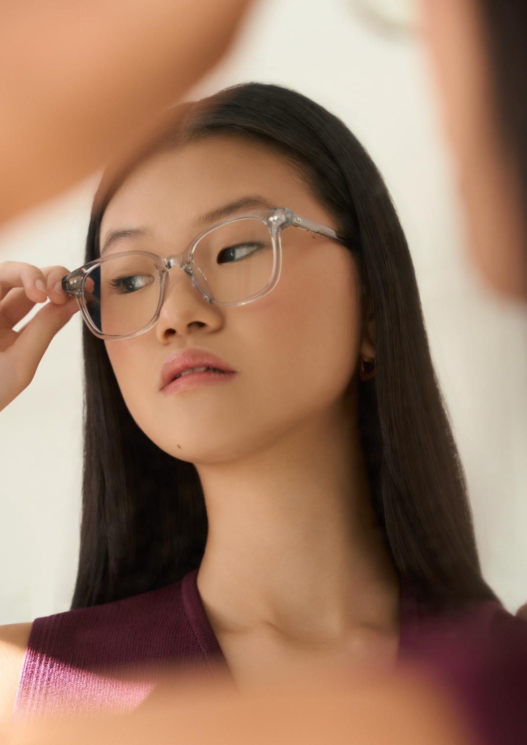 A person with long straight hair looks to the side, wearing KayTran Eyewears Easton - Cloud clear glasses and a burgundy top.