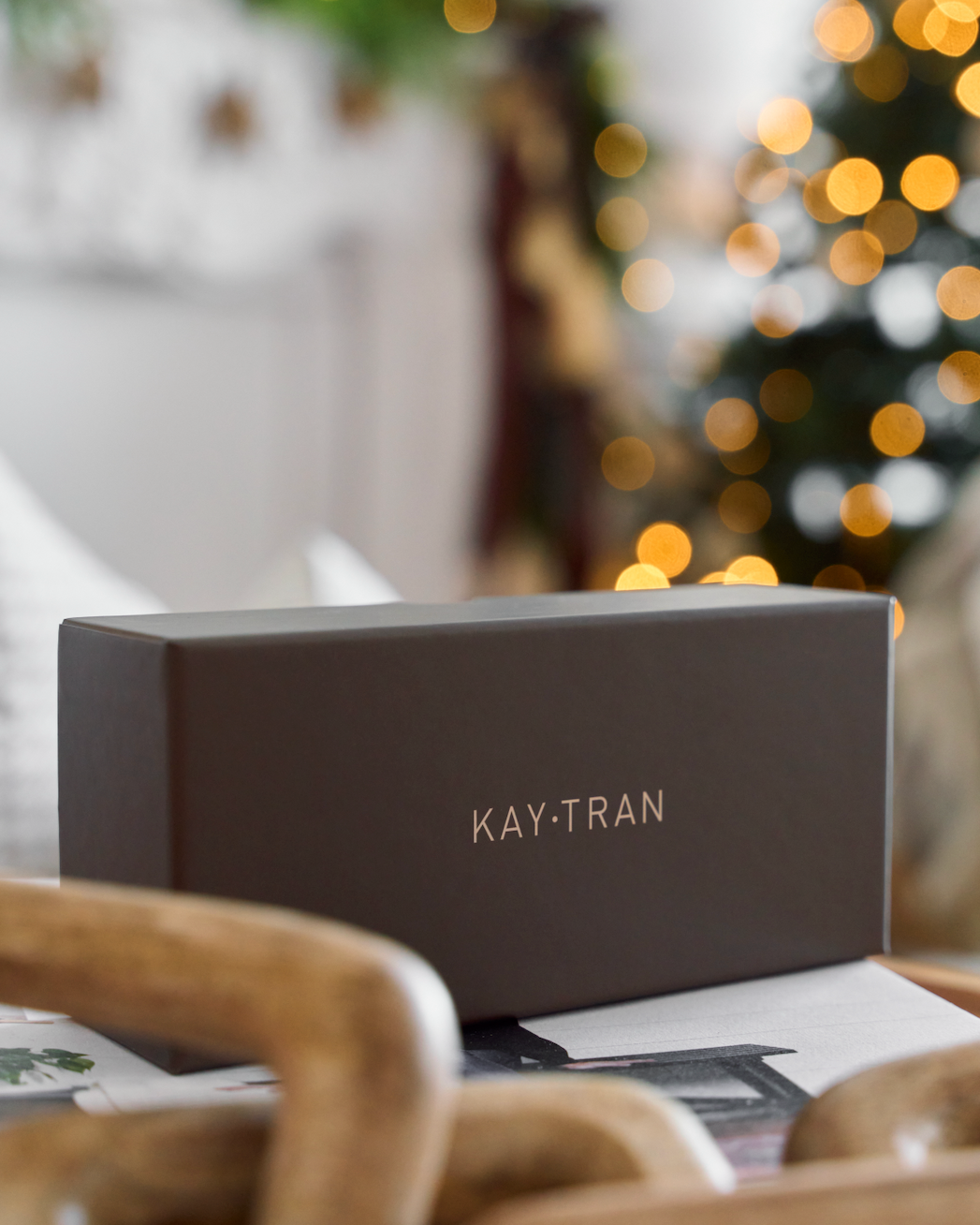 A black KayTran Eyewear Case Set sits on a table with a blurred Christmas tree in the background.