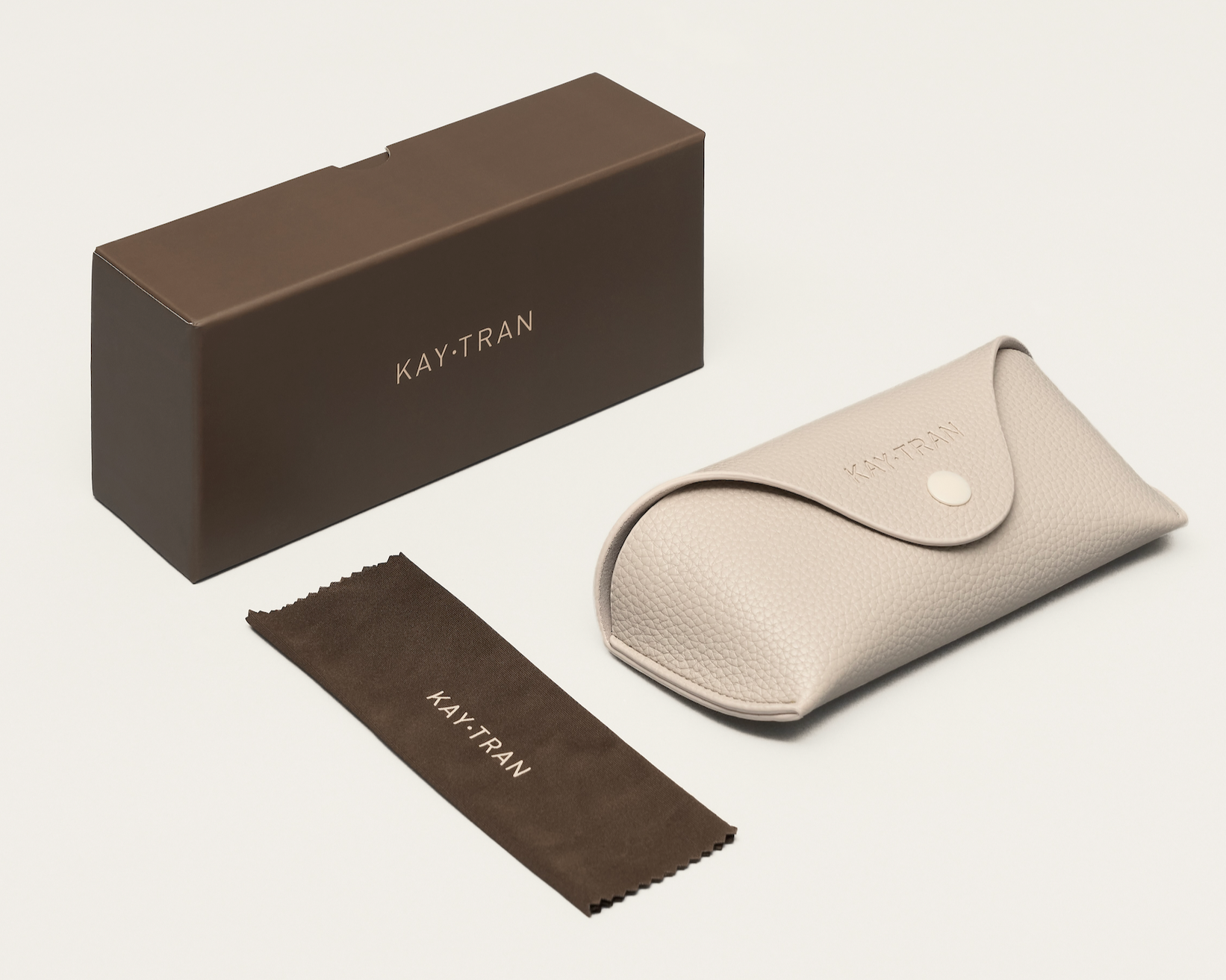 The KayTran Eyewear Case Set includes a brown box, beige case, and brown cloth on a white background.