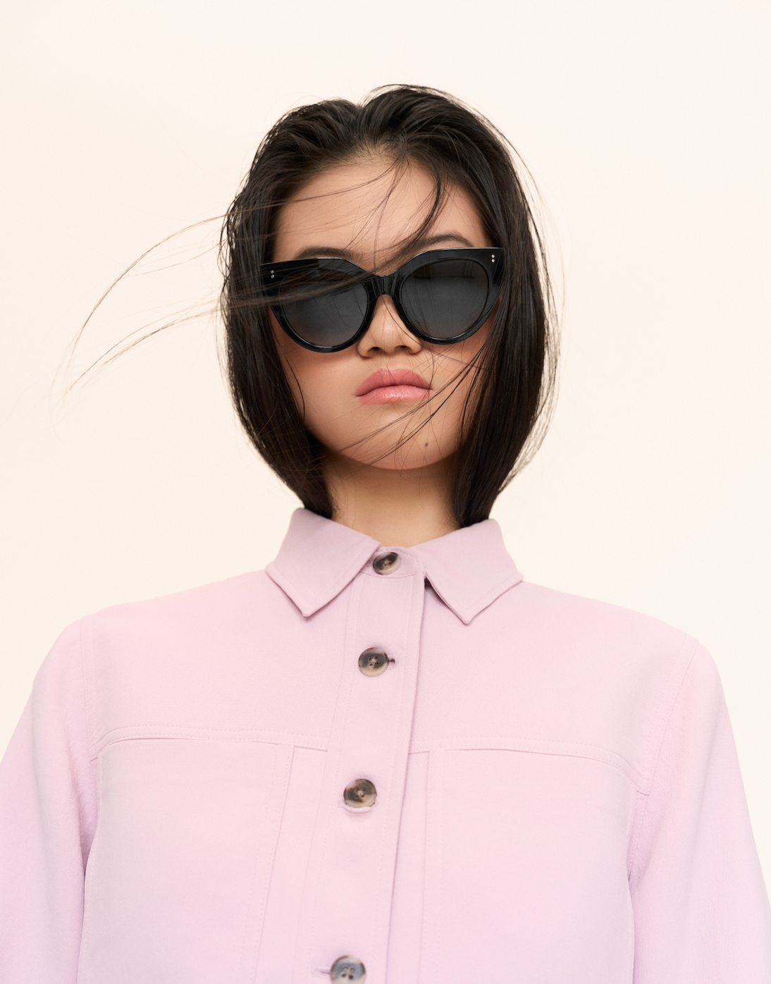 Woman with straight dark hair wears kaytran eyewear Aiden - Polished Black sunglasses and a light pink button-up shirt.