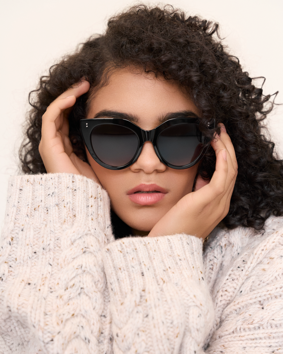 Woman with curly hair wears kaytran eyewears Aiden - Polished Black sunglasses and a cream knit sweater.