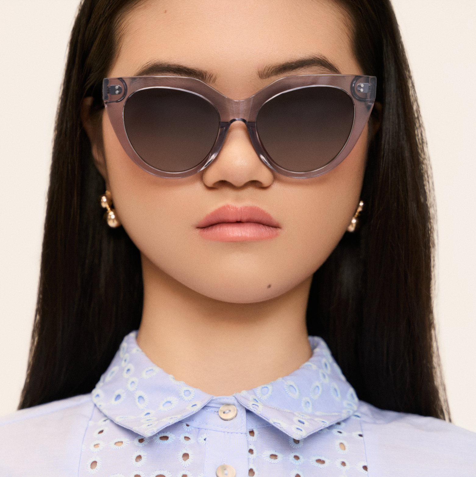 Woman wearing kaytran eyewears Aiden - Slate cat-eye sunglasses, pearl earrings, and a light blue collared shirt.