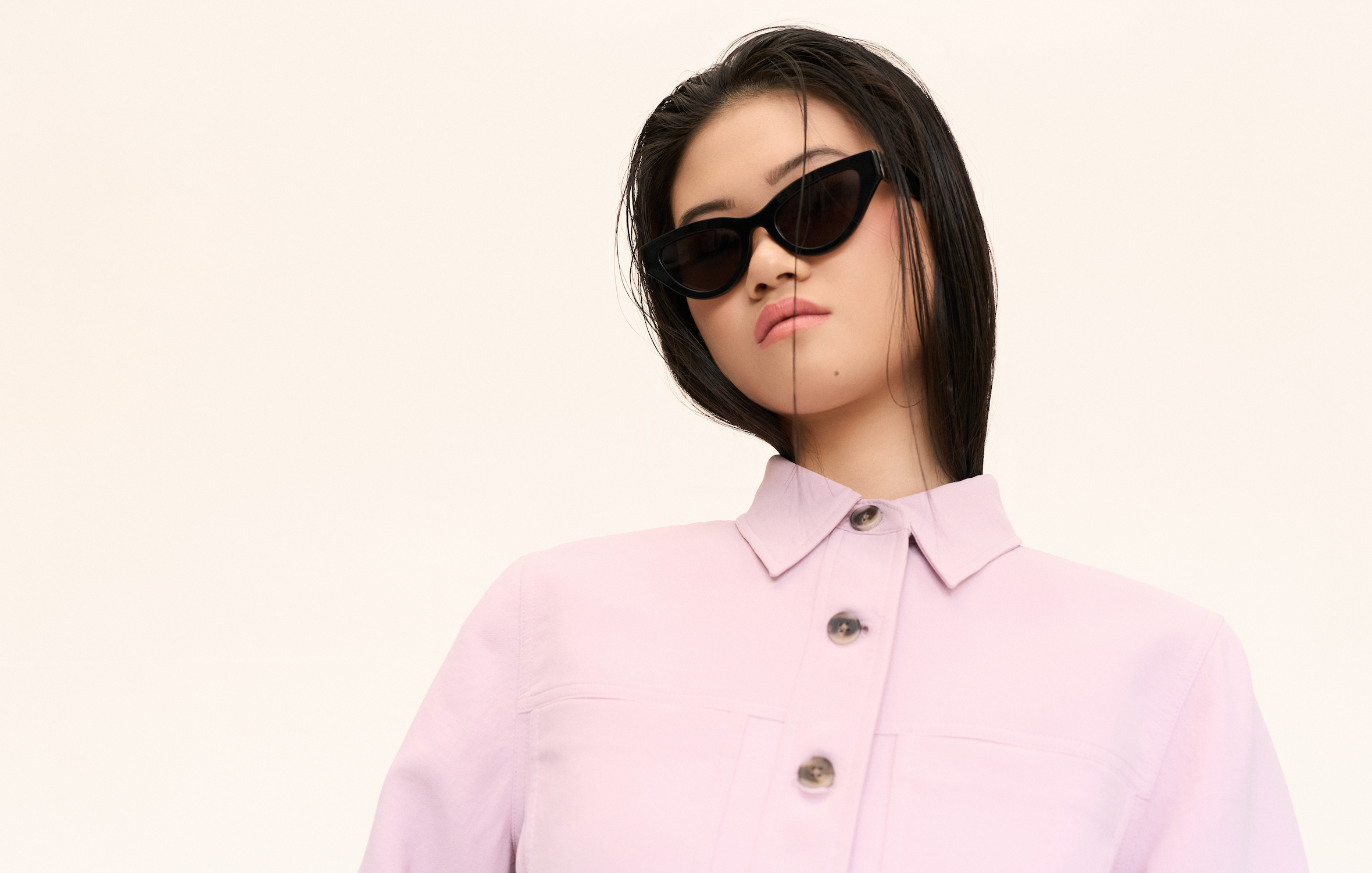Model wears KayTran Eyewear’s Drew - Polished Black sunglasses with a light pink button-up shirt against a plain background.
