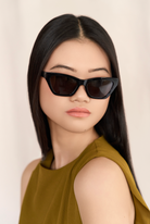 Woman with straight black hair wearing KayTran Eyewears Kai - Polished Black cat-eye sunglasses and an olive top.