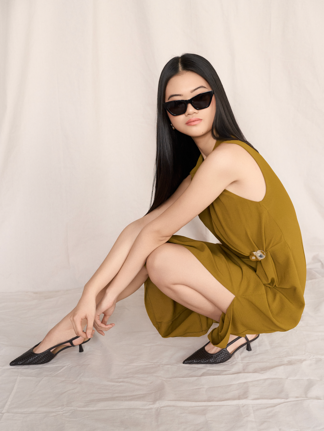 Woman in an olive green dress and black heels sits on the floor, wearing KayTran Eyewears Kai - Polished Black sunglasses.