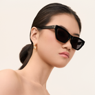 Woman wearing KayTran Eyewears Kai - Polished Black sunglasses, gold earrings, and sleek hair against a neutral background.