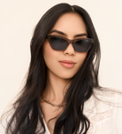Woman with long dark hair wearing KayTran Eyewears Kai - Sage cat-eye sunglasses and a gold chain necklace.